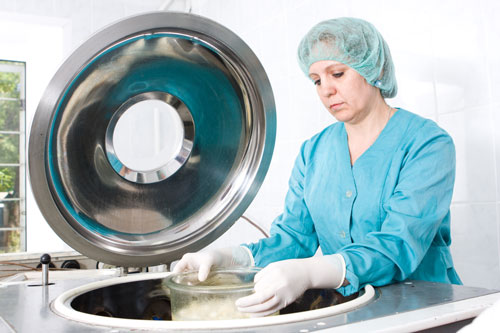 A woman working in a lab with a blue lap coat and gloves at Periodontal Surgical Arts in Austin, TX